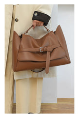 Brown leather handbag held by a person wearing a beige coat.