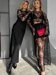 Two women in black lace outfits standing against a gray wall.