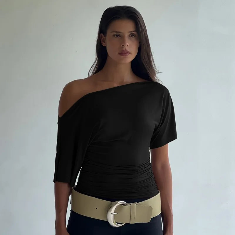 Woman wearing a black one-shoulder top with a beige belt against a plain background