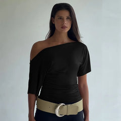 Woman wearing a black one-shoulder top with a beige belt against a plain background