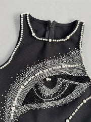 Black sleeveless top with eye design and pearl embellishments on a gray background