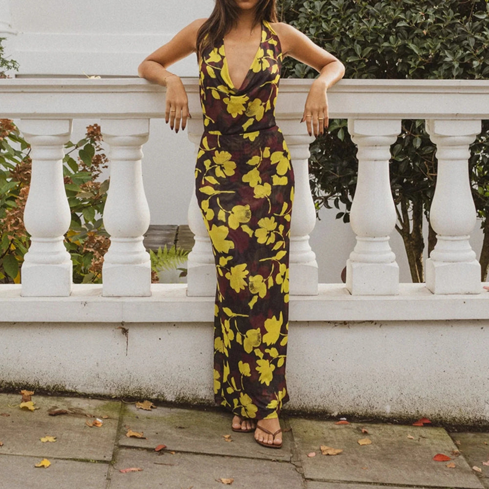 A woman wearing a yellow and brown floral dress is standing against a white railing.