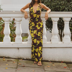A woman wearing a yellow and brown floral dress is standing against a white railing.
