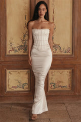 Woman wearing a white strapless gown standing against a decorative wooden wall.