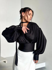 Woman wearing a black blouse with wide sleeves and a white skirt against a plain background