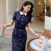 Woman in a navy lace dress holding a bouquet of flowers and a metallic clutch.