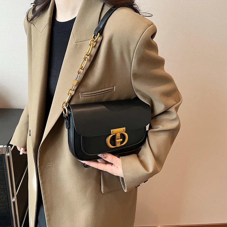 Person holding a black handbag with gold chain strap and clasp, wearing a beige coat.