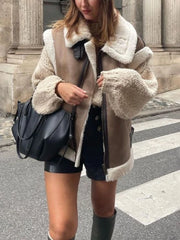 Person wearing a beige shearling coat with a black bag on a city street.