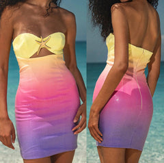 Woman wearing a gradient dress with yellow top and pink to purple skirt on a beach.