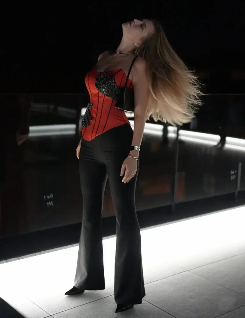 Woman in a red corset and black pants posing in a dark room.