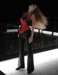 Woman in a red corset and black pants posing in a dark room.