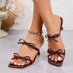 Brown sandals with bow details worn by a person on a light gray surface.