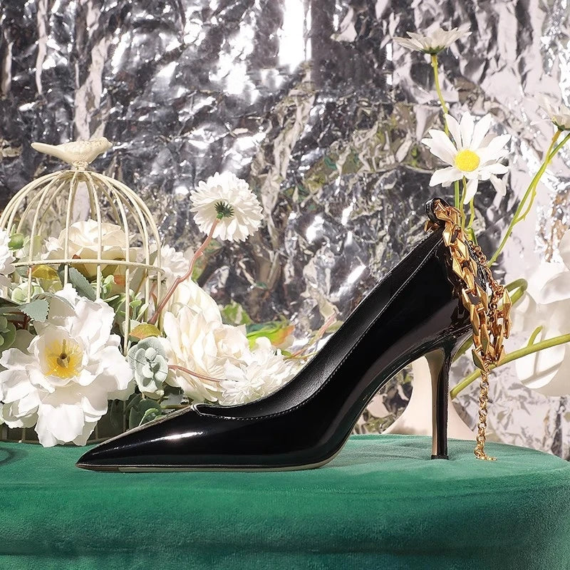 Black high-heeled shoe with gold chain on a green surface with flowers and a metallic background