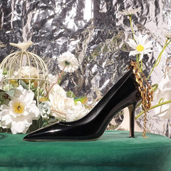 Black high-heeled shoe with gold chain on a green surface with flowers and a metallic background