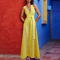 Model wearing a yellow V-neck maxi dress with floral eyelet cut-outs and a tie waist, leaning against a colorful wall.
