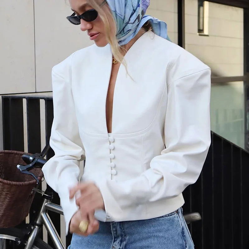 Person wearing a white jacket with a deep neckline and blue jeans, standing outdoors.