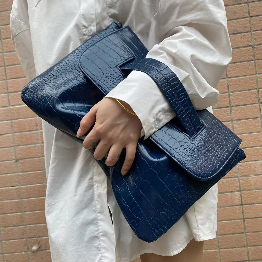 Person holding a blue crocodile-patterned clutch against a brick wall.