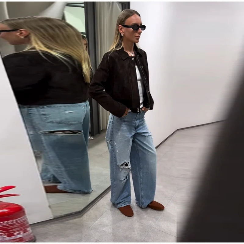Person wearing a black jacket, white shirt, and ripped blue jeans standing in front of a mirror.