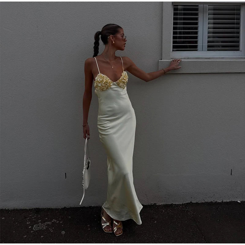 Woman in a white dress with floral details standing against a gray wall.