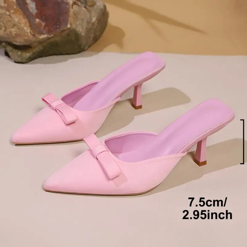 Pair of pink high-heeled shoes with bow details on a beige surface.