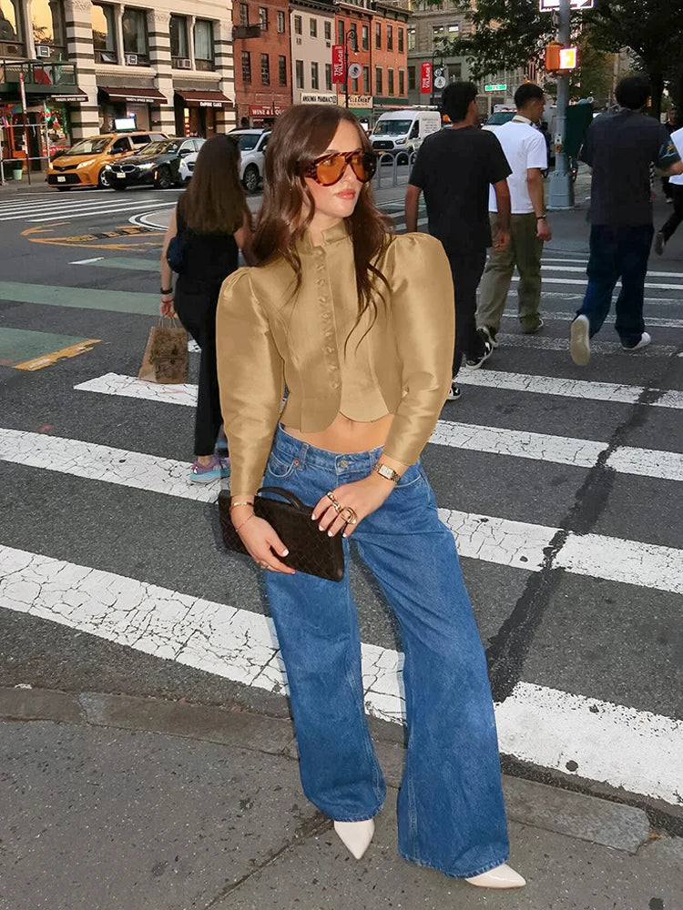 Woman crossing a street wearing a gold blouse and blue jeans.