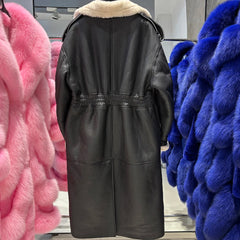 Black leather coat with fur lining displayed against colorful furs in a store setting.