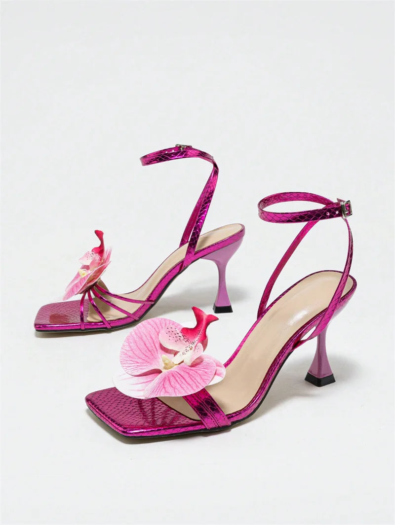 Pair of pink high-heeled sandals with floral decorations on a light gray background