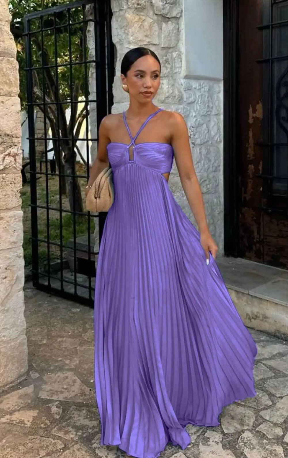 Woman in a purple dress standing outdoors near a stone building.