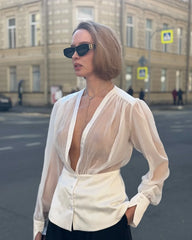 Woman wearing a sheer white blouse and sunglasses on a city street.