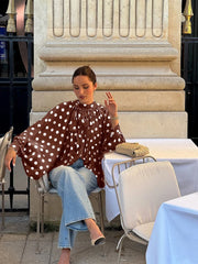 Woman in a polka dot blouse sitting at an outdoor cafe table.