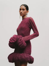 Woman wearing a burgundy dress with ruffled sleeves against a plain background