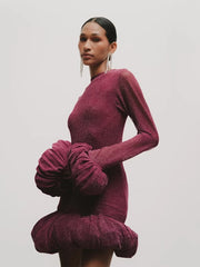 Woman wearing a burgundy dress with ruffled sleeves against a plain background