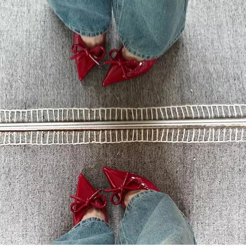 Red shoes with bows worn by a person on a gray carpet.