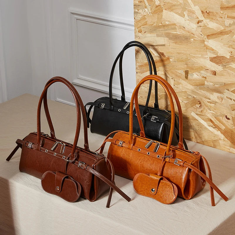 Three handbags in brown and black on a light surface with a wooden wall background