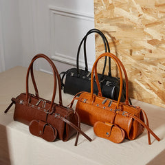 Three handbags in brown and black on a light surface with a wooden wall background
