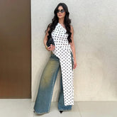 Woman wearing a white polka dot asymmetrical one-shoulder top with a long cascading hem and wide-leg jeans.