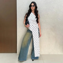 Woman wearing a white polka dot asymmetrical one-shoulder top with a long cascading hem and wide-leg jeans.