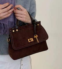 Brown handbag with gold accents held by a person wearing a gray sweater and white pants.