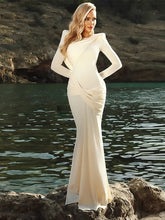 Woman in a white dress standing by a body of water with rocky cliffs.