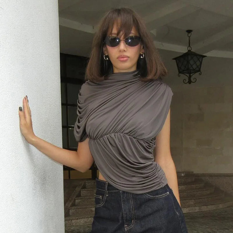Woman wearing a gray top and sunglasses, standing against a white column.