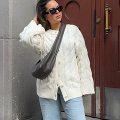 Woman wearing a white cable knit sweater and sunglasses, standing against a red door.