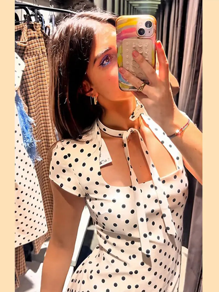 Woman taking a mirror selfie wearing a polka dot dress in a clothing store.