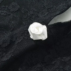 Close-up of a black lace fabric with a white rose flower brooch.