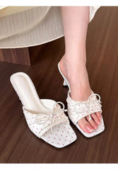 White high-heeled sandals with decorative ribbons on a wooden floor.