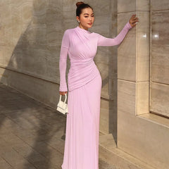 Woman in a pink dress standing against a stone wall.