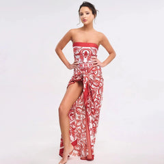 Woman in a red and white printed strapless draped maxi dress against a white background.