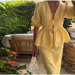 Person wearing a yellow outfit in an outdoor setting with greenery and furniture.