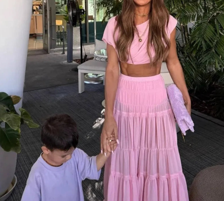 Woman in a pink outfit holding hands with a child outdoors.