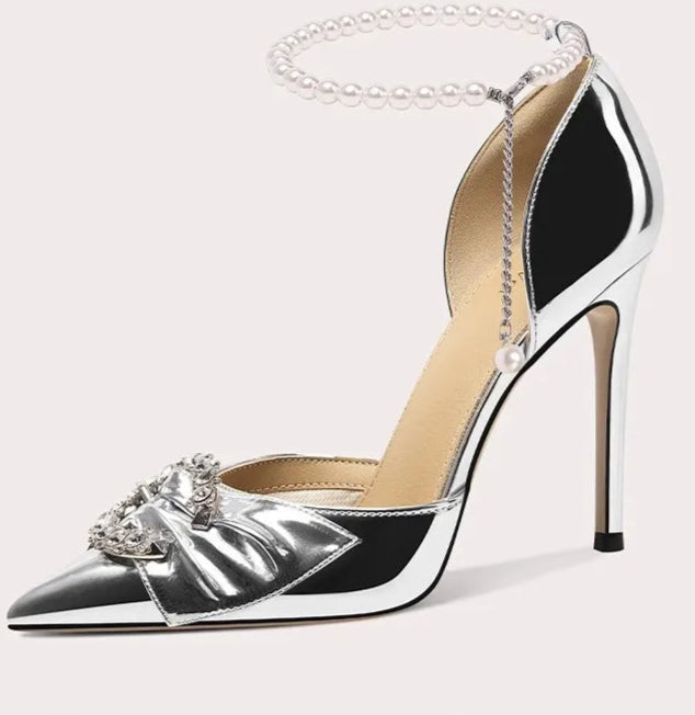 Silver high-heeled shoe with decorative bow and chain on a white background