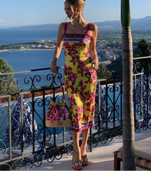 Woman in a colorful dress standing on a balcony with a scenic view of the sea and mountains.